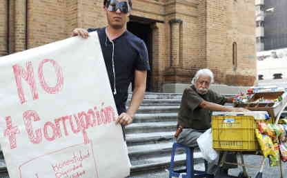 Un hombre que usa un antifaz sostiene un cartel en el que se lee no más corrupción.
