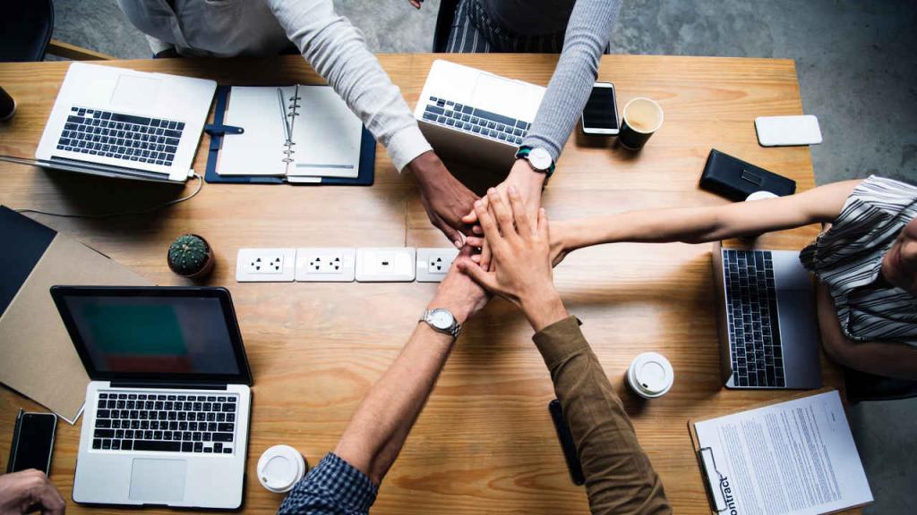 Un grupo de personas entrelazan sus manos sobre una mesa de trabajo.