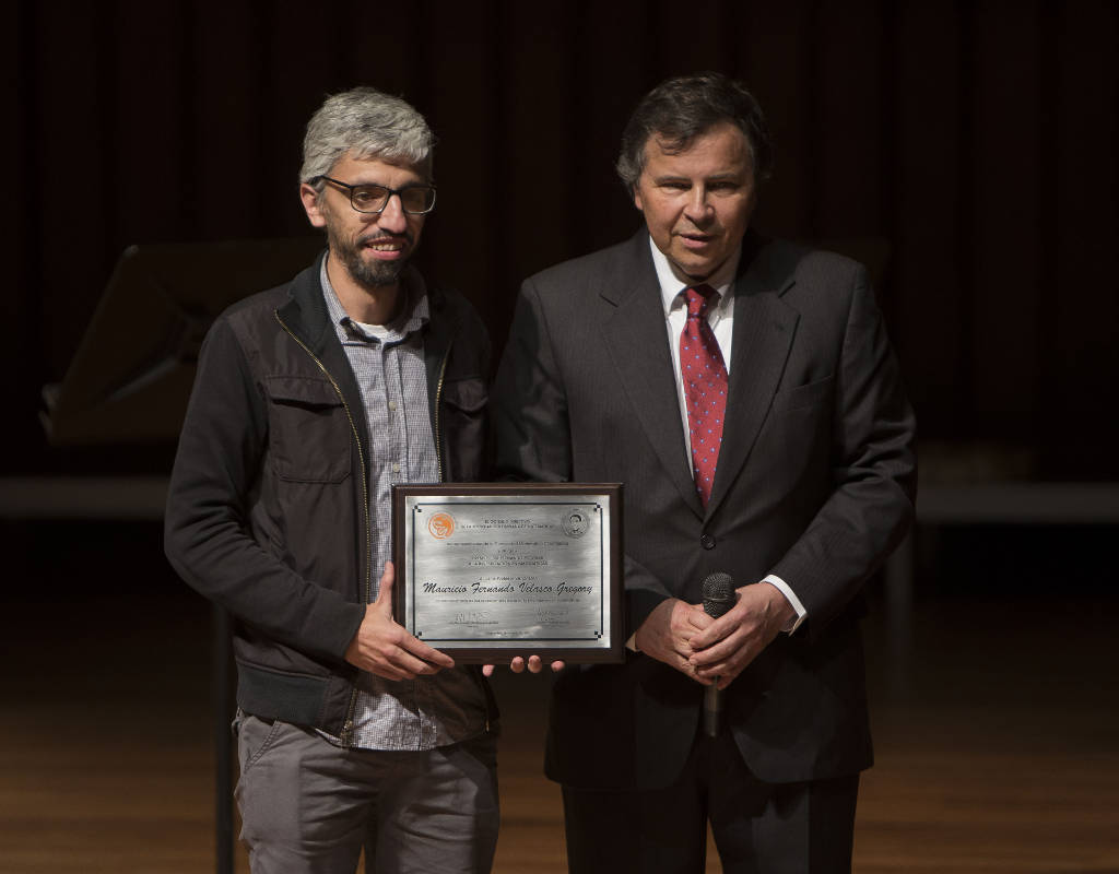 El profesor Mauricio Velasco recibe una placa con el reconocimiento por su trabajo investigativo. 