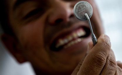 Un hombre se mira los dientes a través de un espejo de odontología.