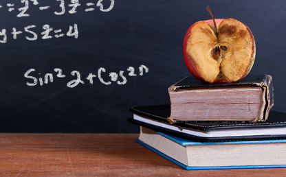 Una manzana podrida sobre dos libros frente a un tablero con signos matemáticos. 