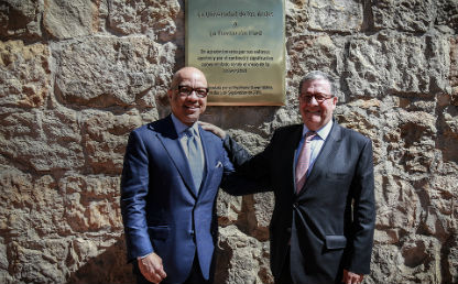 dos hombres estrechan brazos con señal de agradecimiento, se ve una placa detrás de ellos 