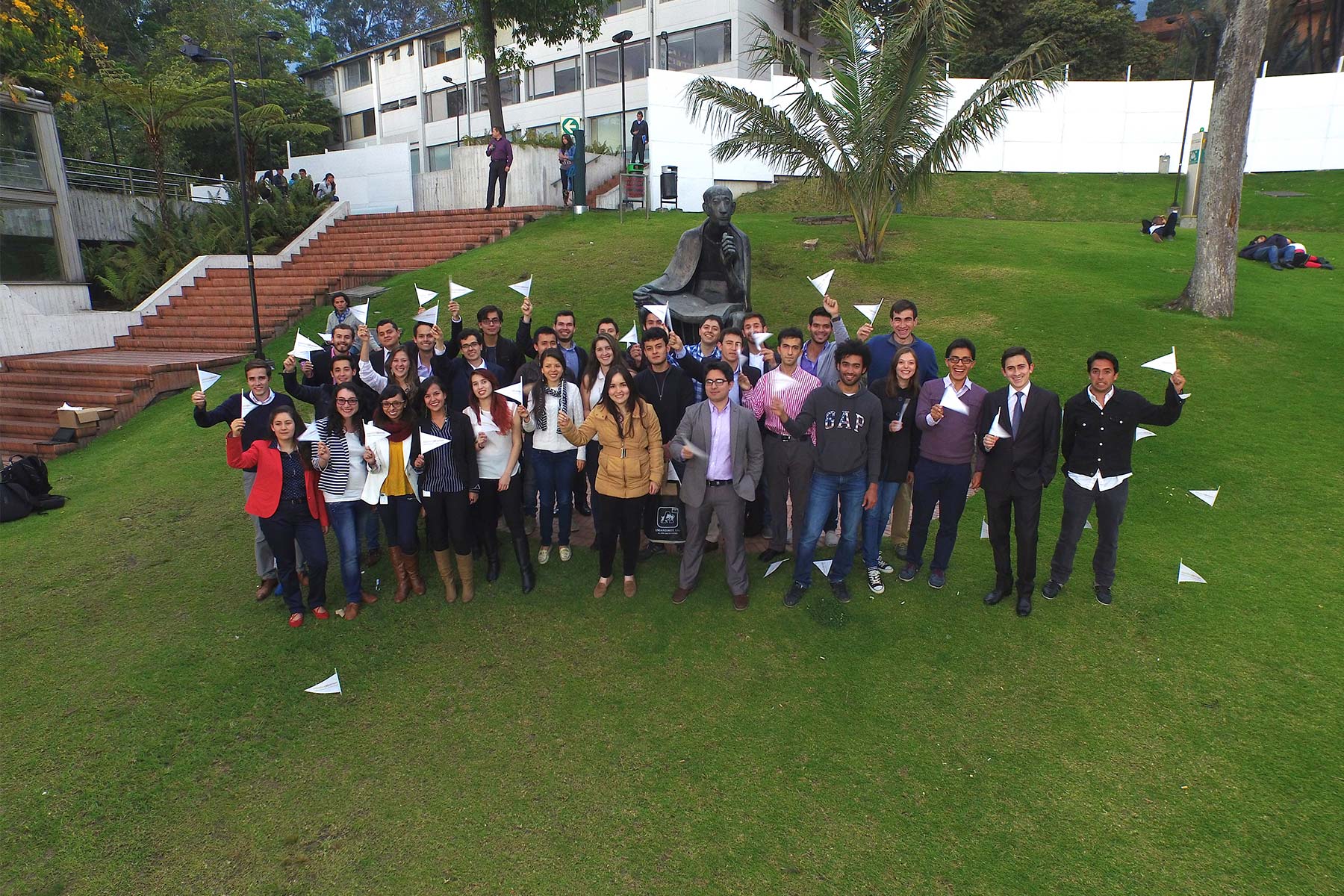 Grupo de egresados Uniandes en el prado Alberto Magno de la Universidad elevan sus manos en señal de saludo.