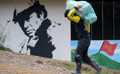 Hombre caminando por una calle destapada y cargando un paquete muy pesado. 